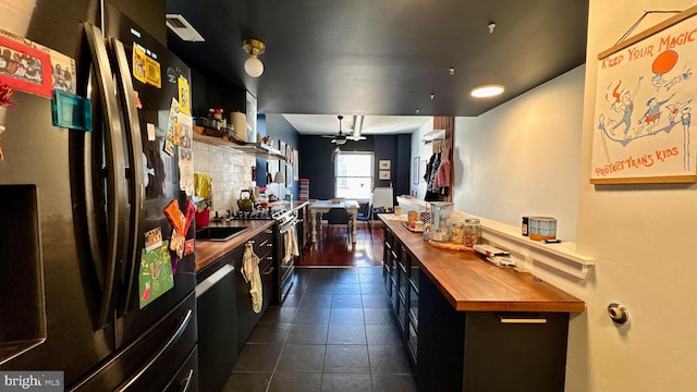 kitchen with stainless steel range with gas stovetop, freestanding refrigerator, dark cabinets, butcher block counters, and dark tile patterned floors