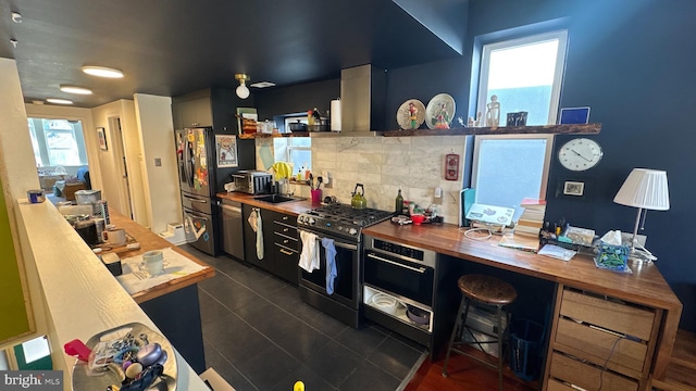 kitchen with a sink, butcher block counters, dark tile patterned flooring, tasteful backsplash, and appliances with stainless steel finishes
