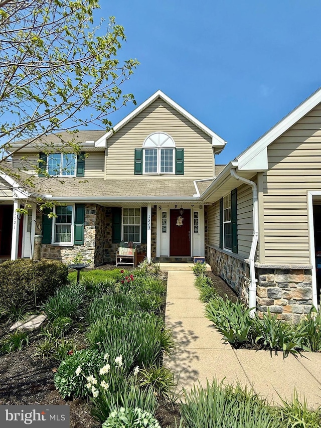 traditional-style home with a shingled roof, covered porch, and stone siding
