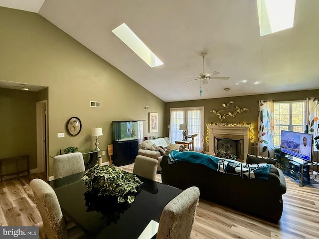 living area featuring visible vents, high vaulted ceiling, a ceiling fan, light wood finished floors, and a skylight