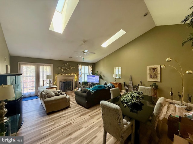 living area with a fireplace, ceiling fan, high vaulted ceiling, light wood-type flooring, and a skylight