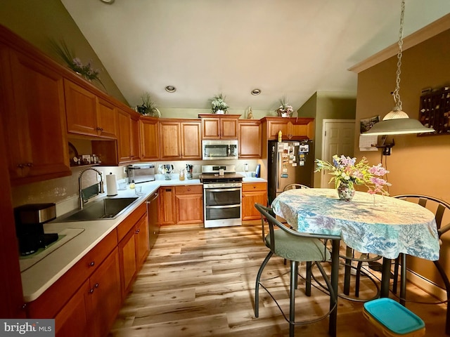 kitchen featuring pendant lighting, appliances with stainless steel finishes, vaulted ceiling, light wood-type flooring, and a sink