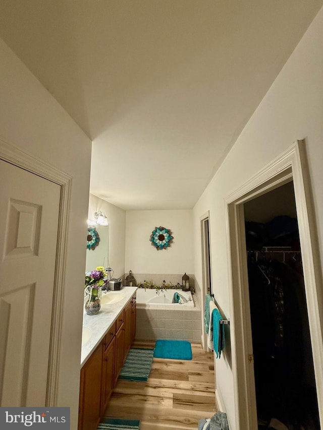 full bathroom featuring double vanity, a spacious closet, wood finished floors, and a garden tub