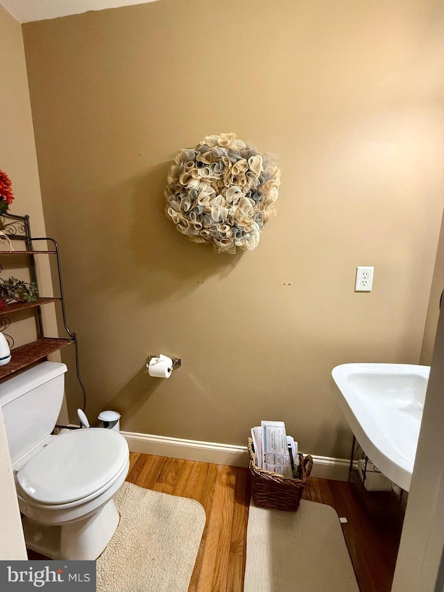 bathroom featuring toilet, baseboards, a sink, and wood finished floors