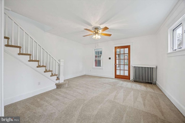 interior space featuring radiator, baseboards, carpet, a ceiling fan, and stairs
