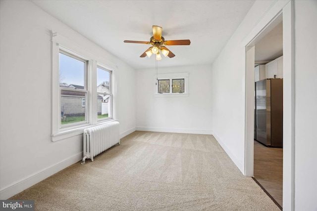 spare room with radiator heating unit, light carpet, a ceiling fan, and baseboards