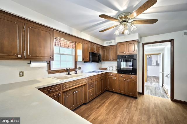 kitchen with light countertops, wood finished floors, a sink, and black appliances