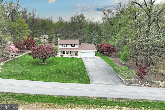 traditional-style house featuring driveway, covered porch, an attached garage, a view of trees, and a front yard