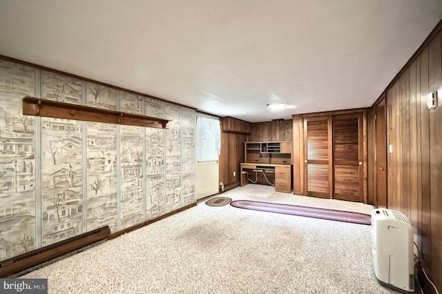 unfurnished living room with a baseboard heating unit, built in study area, carpet floors, and wood walls