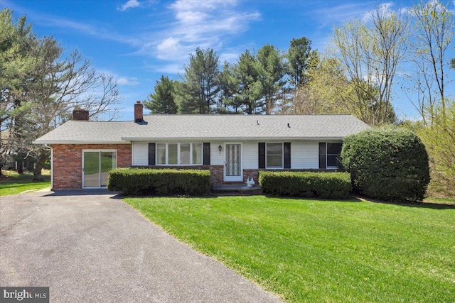 ranch-style home with brick siding, a chimney, a front yard, and aphalt driveway