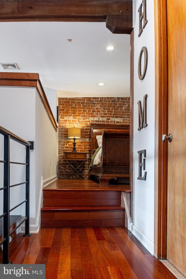 stairs with hardwood / wood-style floors, brick wall, baseboards, and visible vents