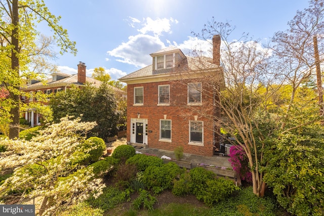 view of side of property with a chimney, a patio area, and brick siding