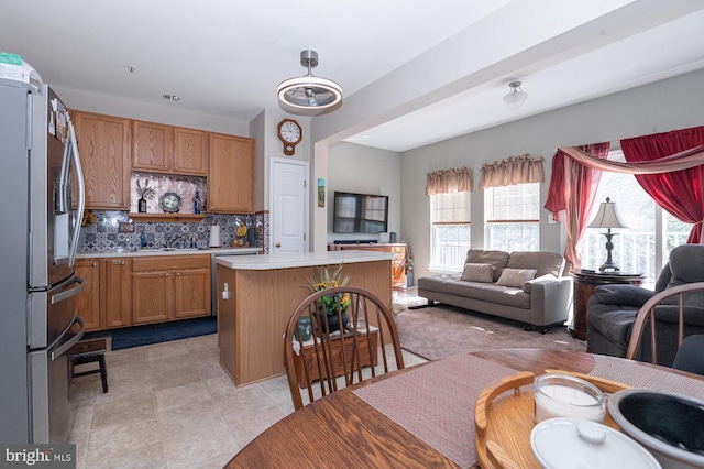 kitchen featuring a kitchen island, open floor plan, stainless steel refrigerator with ice dispenser, light countertops, and tasteful backsplash