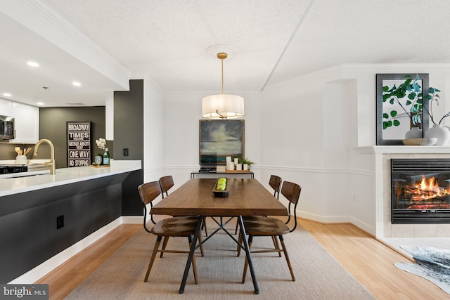 dining area featuring light wood-style floors, baseboards, recessed lighting, ornamental molding, and a tiled fireplace