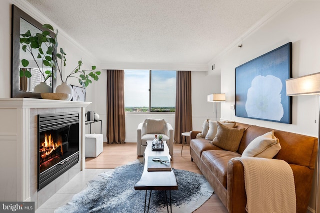 living room featuring a tiled fireplace, ornamental molding, and a textured ceiling