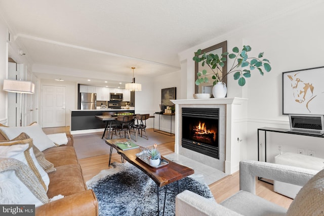 living room featuring a tile fireplace, crown molding, and light wood-style flooring