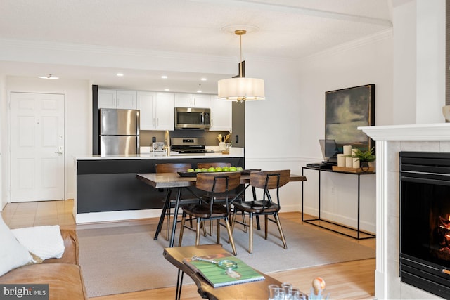dining space with a tiled fireplace, recessed lighting, light wood-style floors, baseboards, and crown molding