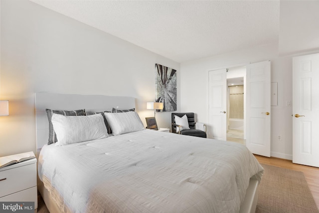 bedroom with ensuite bathroom, a textured ceiling, baseboards, and light wood-type flooring