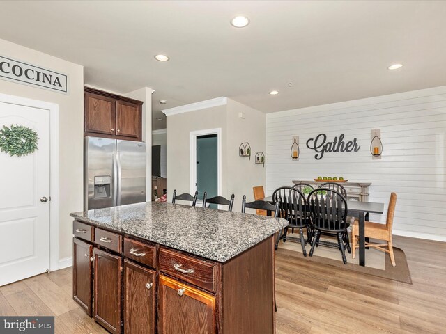 kitchen with light wood-style flooring, stainless steel refrigerator with ice dispenser, light stone countertops, a kitchen island, and recessed lighting