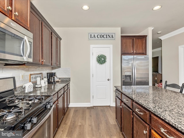 kitchen featuring dark stone counters, baseboards, wood finished floors, and stainless steel appliances