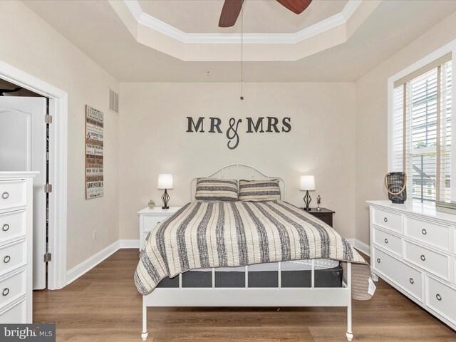 bedroom with a raised ceiling, wood finished floors, visible vents, and crown molding