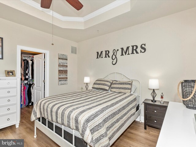 bedroom with a spacious closet, a raised ceiling, wood finished floors, visible vents, and a closet