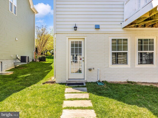 entrance to property featuring a lawn, brick siding, and cooling unit