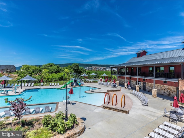 community pool with a patio area, a water slide, and fence