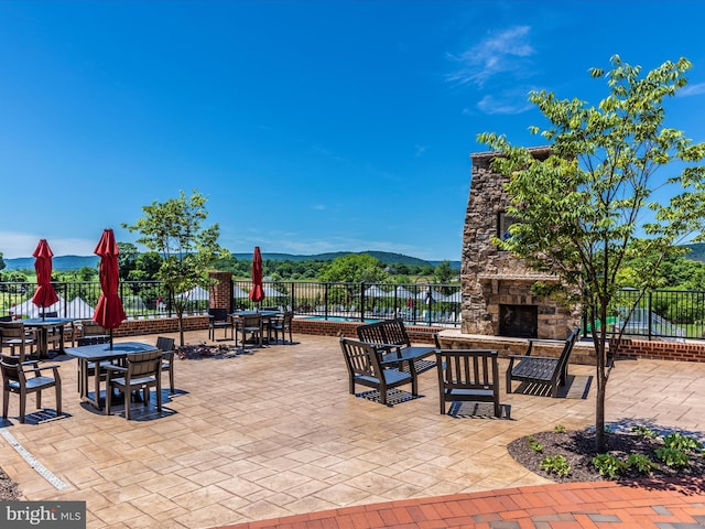view of patio / terrace with fence, an outdoor stone fireplace, and a mountain view
