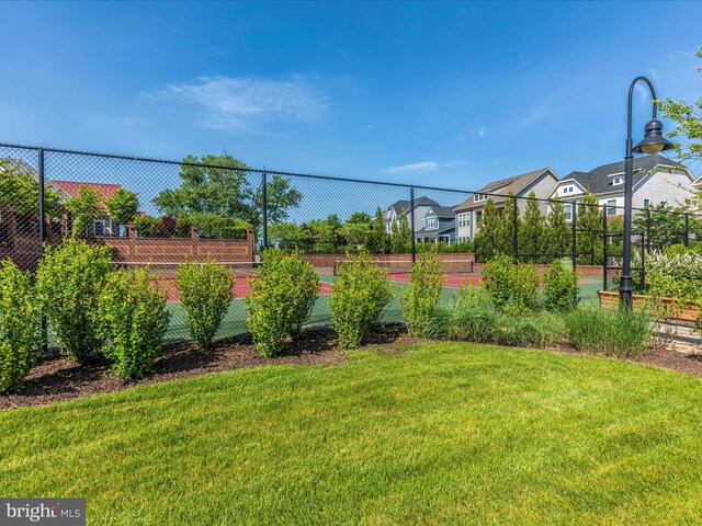 view of yard with fence, a residential view, and a tennis court