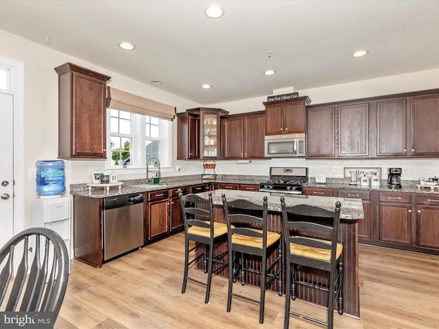 kitchen with dark brown cabinets, light wood-type flooring, stone counters, appliances with stainless steel finishes, and a breakfast bar area