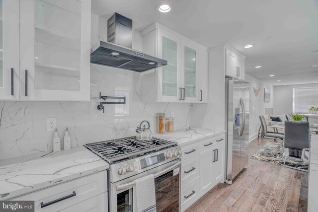 2832 Edgemont St, Philadelphia, PA 19134 - kitchen with wall chimney exhaust hood, stainless steel appliances, light wood-style flooring, white cabinets, and light stone countertops