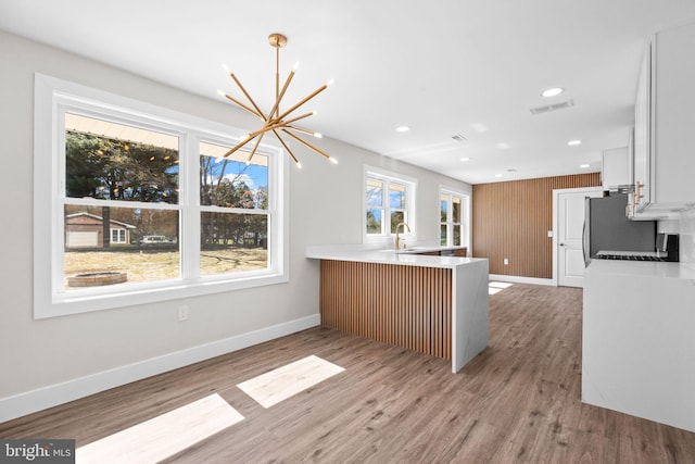kitchen with visible vents, a sink, baseboards, a peninsula, and a chandelier