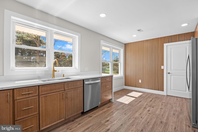 kitchen with brown cabinets, appliances with stainless steel finishes, a sink, light countertops, and light wood-style flooring