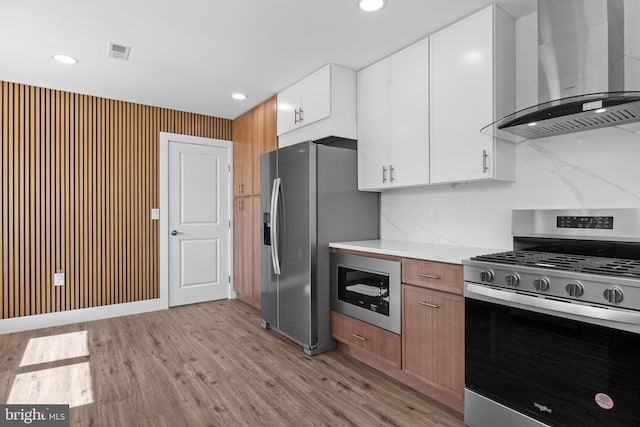 kitchen with wall chimney range hood, visible vents, light countertops, light wood finished floors, and stainless steel appliances