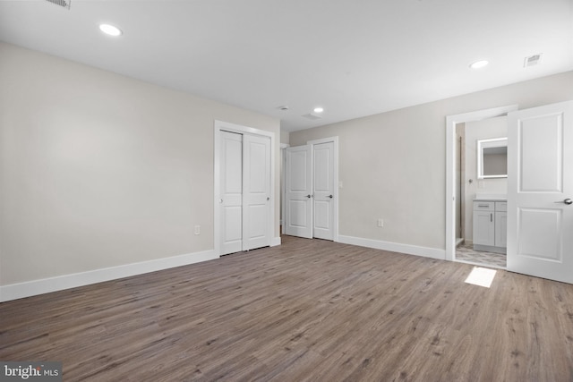 unfurnished bedroom with baseboards, ensuite bathroom, and wood finished floors