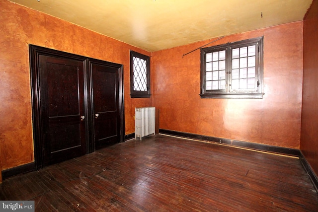 unfurnished bedroom with radiator, baseboards, wood-type flooring, and multiple windows