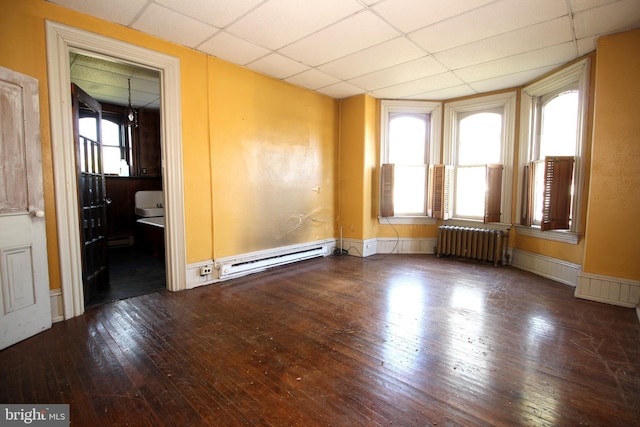 empty room with a baseboard radiator, radiator heating unit, wood-type flooring, and a paneled ceiling
