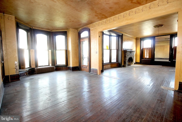 unfurnished living room featuring radiator, wood-type flooring, and a stone fireplace