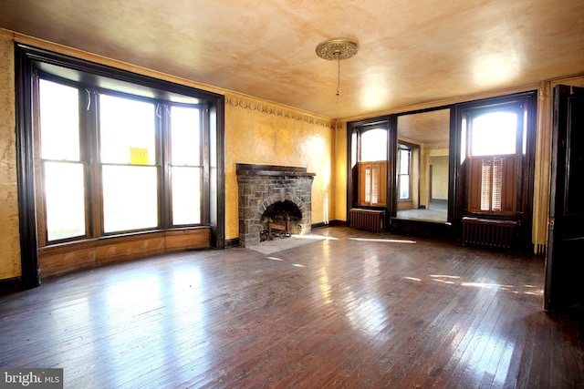 unfurnished living room featuring radiator, a healthy amount of sunlight, wood-type flooring, and a stone fireplace