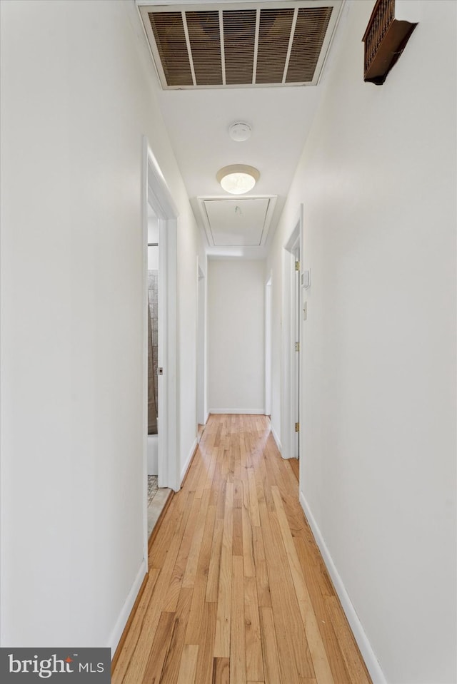 hallway with visible vents, attic access, baseboards, and light wood-type flooring