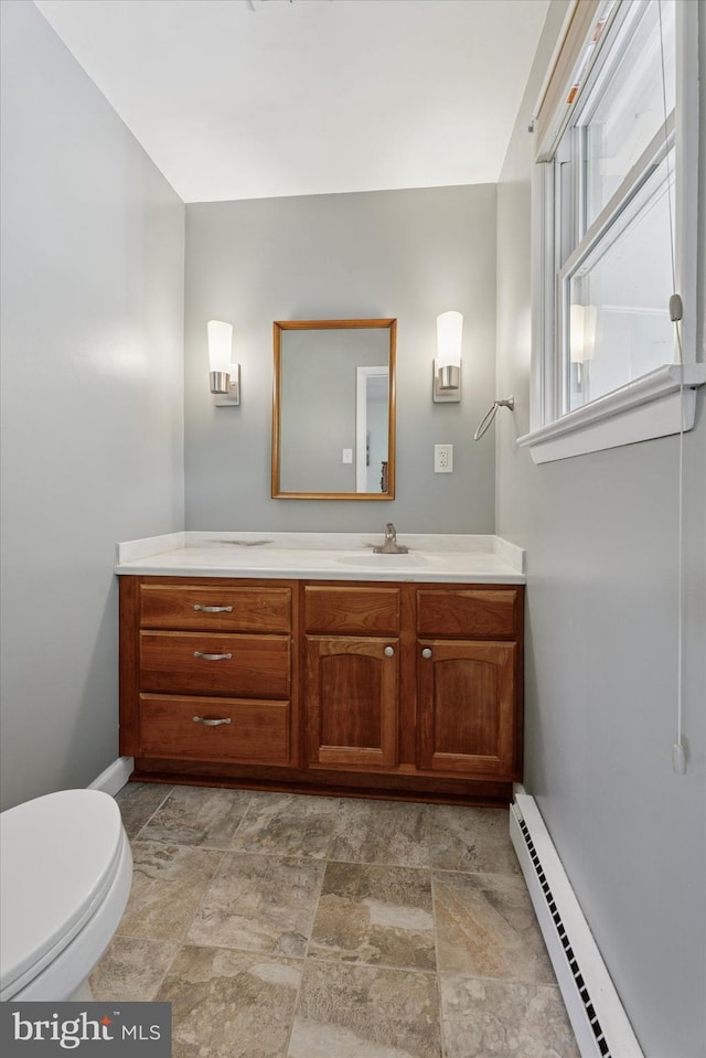 half bathroom with stone finish floor, vanity, baseboards, a baseboard heating unit, and toilet