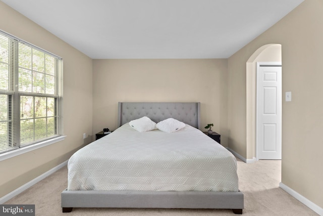 bedroom featuring baseboards, arched walkways, and light carpet