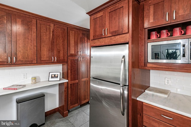 kitchen with brown cabinetry, light countertops, tasteful backsplash, appliances with stainless steel finishes, and light tile patterned floors