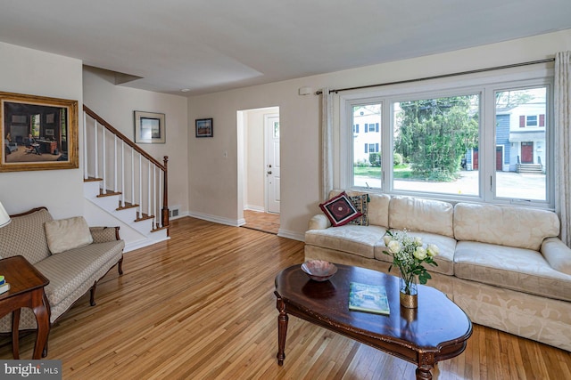 living area with light wood-type flooring, baseboards, visible vents, and stairway