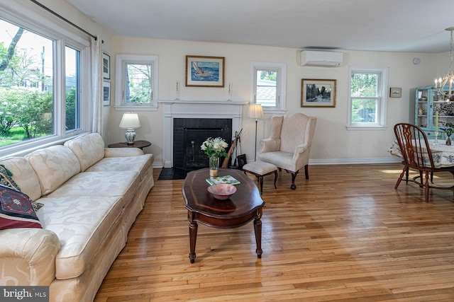 living room with a fireplace with flush hearth, baseboards, an AC wall unit, light wood finished floors, and a notable chandelier