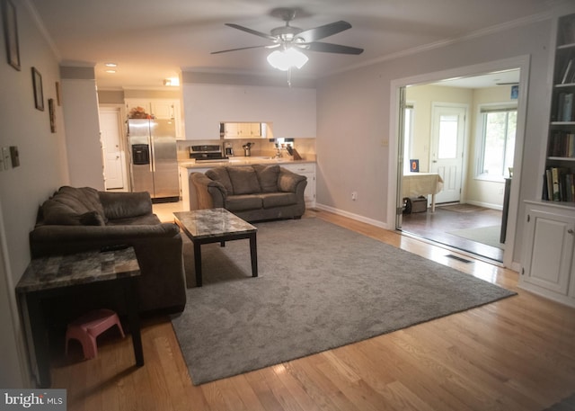 living area featuring crown molding, a ceiling fan, light wood-style floors, and baseboards