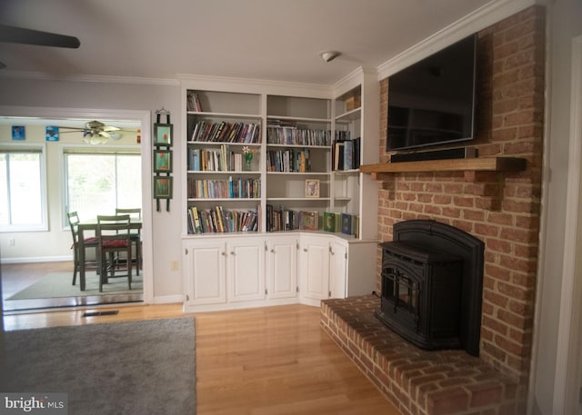 sitting room with ceiling fan, a wood stove, light wood-style flooring, baseboards, and ornamental molding