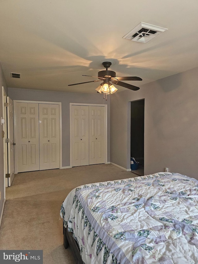 carpeted bedroom featuring visible vents, a ceiling fan, and multiple closets