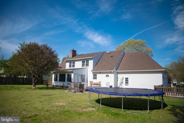 rear view of property with fence, a trampoline, a chimney, and a lawn
